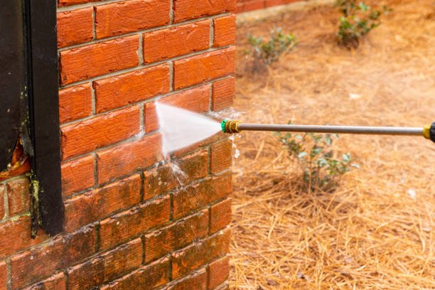 Pressure washer using water to clean a dirty brick wall on a house